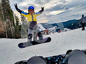 man sitting at snowed hill with snowboard happy woman jumping in front