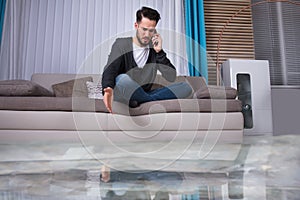 Man Sitting On Sofa Calling To Plumber