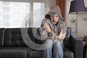 Man is sitting on sofa at home and feeling cold. photo