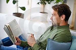 Man sitting on sofa and reading book at home, lockdown concept.