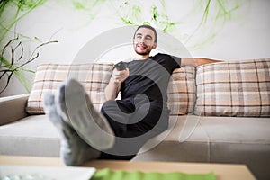 Man sitting on a sofa watching tv holding remote control at home