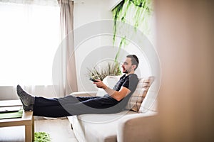 Man sitting on a sofa watching tv holding remote control at home