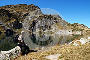 Man sitting on a stone admiring a mountain lake