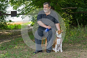 Man sitting on a stool next to his four-legged friend basenji dog in summer park