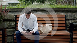 Man sitting on a street bench with packagings with fast food, using smartphone