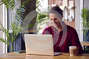 Man Sitting At Table In Coffee Shop Working On Laptop Computer