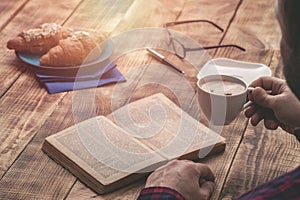 Man sitting at table relaxing reading book and drinking coffee