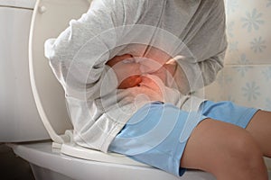 Man sitting on toilet and holding his stomach with stomach pain causes of gastritis or constipation with red dot in bathroom and