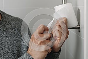 man sitting in the toilet taking a piece of paper