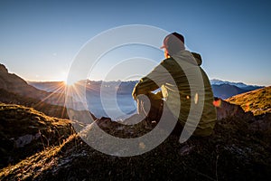 Man sitting on a top of mountain and watching the sunset
