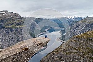 Man sitting on Trolltunga rock and looking at Norwegian mountain landscape