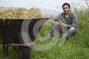 Man sitting beside wheelbarrow with hay in field portrait