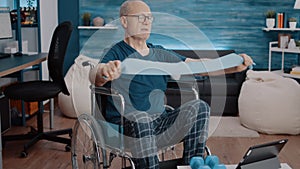 Man sitting in wheelchair and doing exercise with resistance band