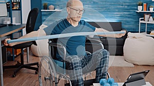 Man sitting in wheelchair and doing exercise with resistance band