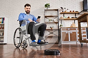 Man sitting in a wheelchair and using a robotic vacuum connected with a phone