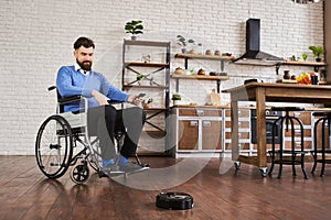 Man sitting in a wheelchair and using a robotic vacuum connected to his phone