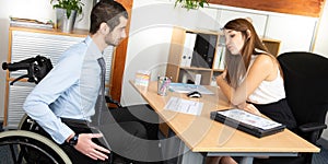 Man Sitting In Wheelchair Working In Modern Office having discussion with female colleague