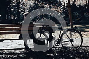 Man sitting on a wooden bench next to a bicycle in a city park