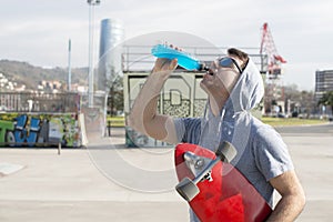 Man with skateboard drinking energy drink after sport.