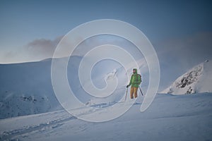 man skier in bright ski suit stands and looks up