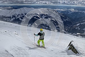 Muž lyžiar hľadajúci najlepšiu trať pre freeride. Lyžiar, ktorý sa pozerá dole do údolia. Žltá prilba. Čakanie na správnu chvíľu.