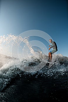 man skilfully riding wave on the wakesurf on the background of blue sky