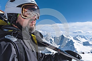 A man with skis stands high in the mountains enjoying the scenery. Go downhill skiing, extreme relaxation