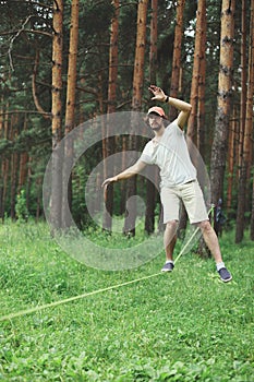 Man slacklining walking and balancing on a rope, slackline outdoors in forest