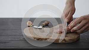 Man slcing small cured sausage on olive board with copy space