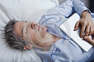 Man sleeping on bed with holding a digital tablet