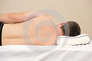 The man sleeps on his side on an orthopedic pillow made of memory foam, viewed from behind, from behind. Correct