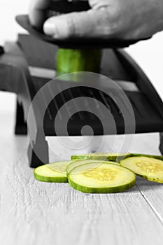 Man slicing cucumber with a mandoline on a grey wood kitchen worktop