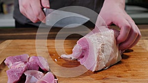 Man slicing pork meat on a table, working process closeup. Kitchen, knife.