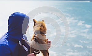 Man with small golden japanese shiba inu dog sitting togetherness on a mountain and looking at blue sea horizon, friends on relax