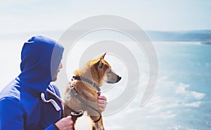 Man with small golden japanese shiba inu dog sitting togetherness on a mountain and looking at blue sea horizon, friends on relax