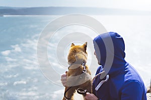 Man with small golden japanese shiba inu dog sitting togetherness on a mountain and looking at blue sea horizon, friends on relax