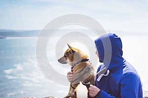 Man with small golden japanese shiba inu dog sitting togetherness on a mountain and looking at blue sea horizon, friends on relax