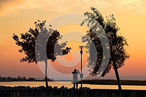 Man with smart phone while taking a picture of warm coloured twilight sky over the Neusiedl lake in Austria