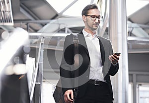 Man on smart phone - young businessman in airport. Handsome men in eyeglasses wearing suit jacket indoors