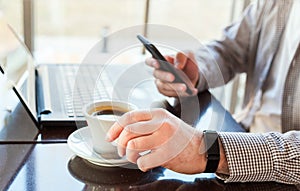 Man in smart watch drinking coffee on work space. Man using laptop, holding smart phone for business work or study. Close up smart