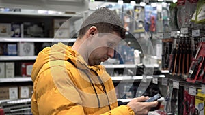 A man with a smartphone in a building supermarket. A man chooses a product in a hardware store