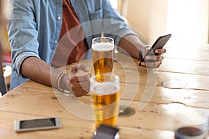Man with smartphone drinking beer at bar or pub