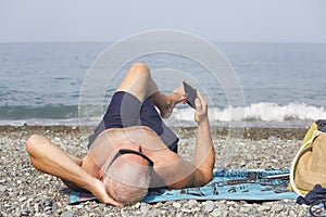 A man with a smartphone in his hand is lying on a pebble beach.