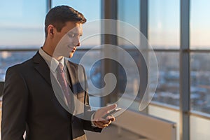 Man with smartphone standing in modern office interior.