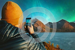 Man with smartphone taking photo of northern lights winter travel in Norway adventure vacations outdoor