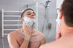 Man smearing foam for shave on his face in the bathroom