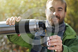 Man with smile pours a hot drink - tea or coffee from thermos in