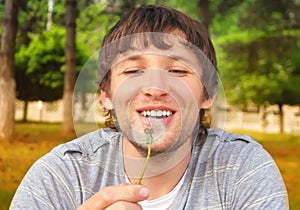 Man smiling and blowing Dandelion