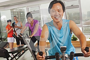 Man smiling and exercising on the exercise bike at the gym, looking at camera