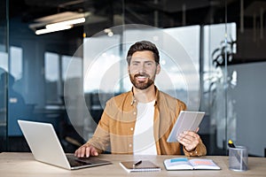 Man smiling multitasking using laptop and tablet in office